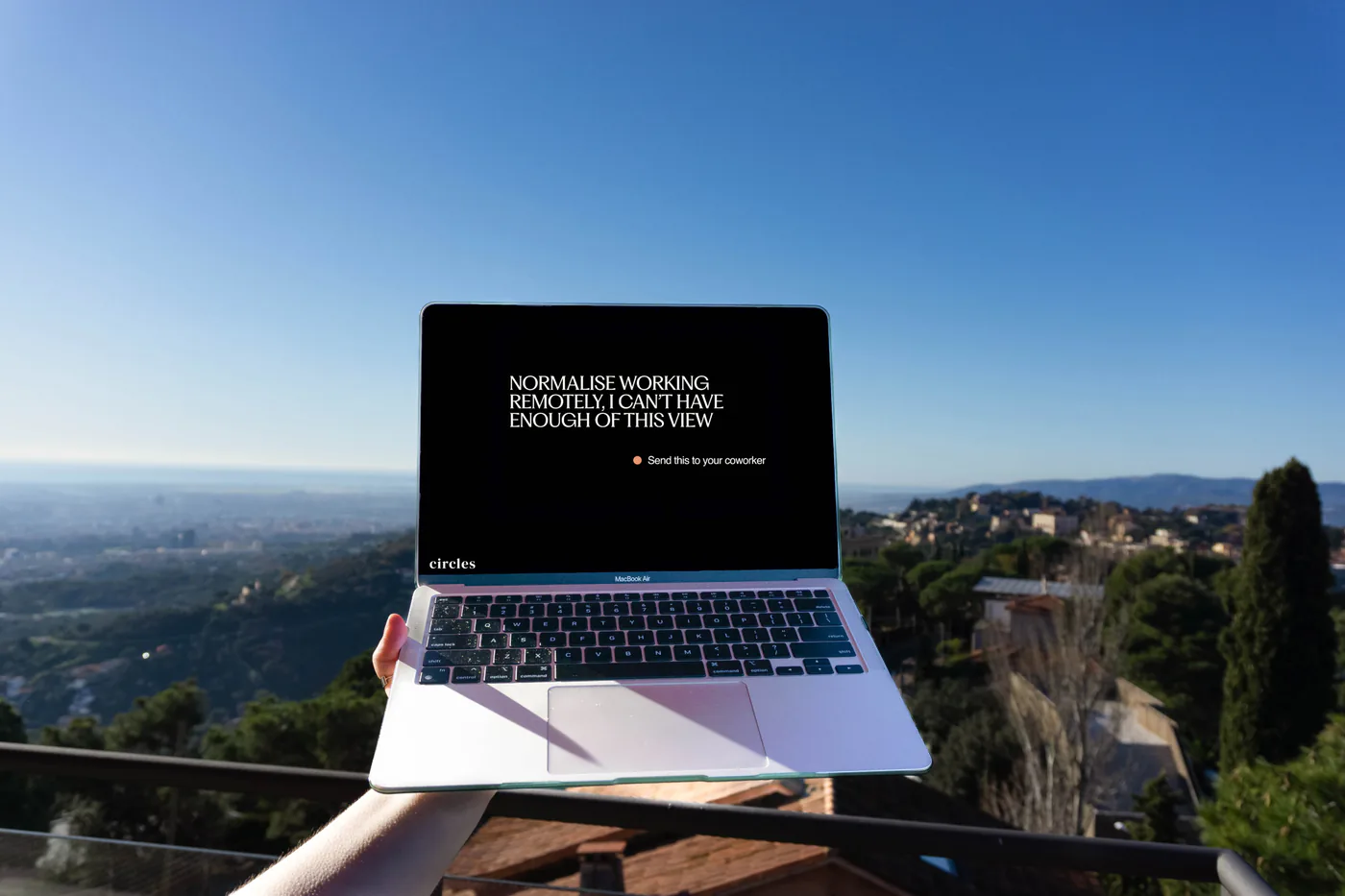 A laptop held up against the view over Barcelona from the house terrace, its screen reading normalise working remotely, I can't have enough of this view.