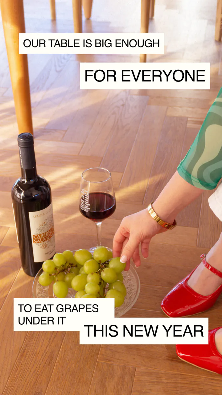 Instagram story: grapes, wine and a hand reaching for the plate under the house table, captioned our table is big enough for everyone to eat grapes under it this New Year.